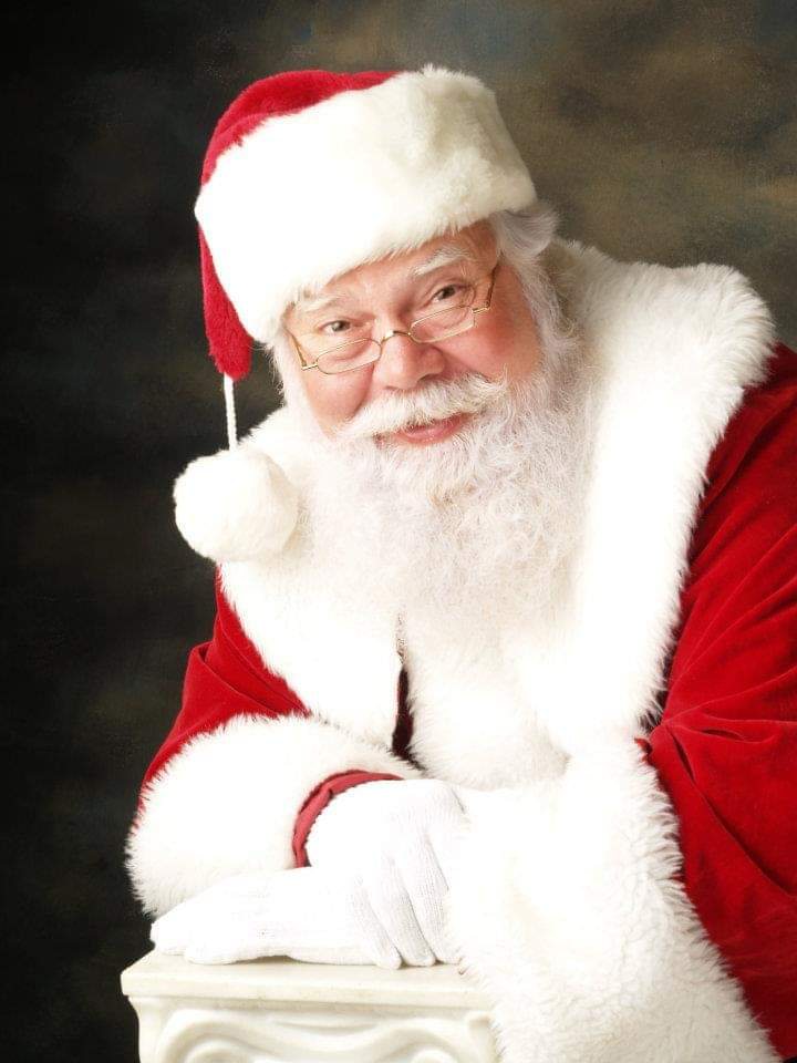 Studio portrait of Santa John smiling warmly, leaning on a white pillar
